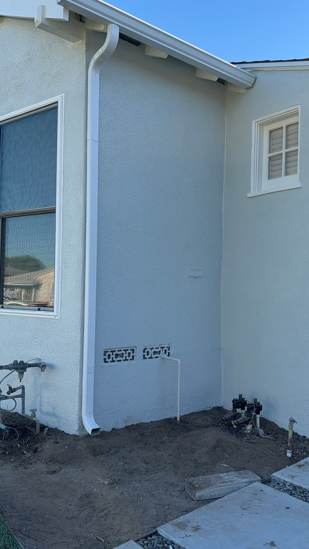 White downspout routed to grade beside a freshly painted stucco house